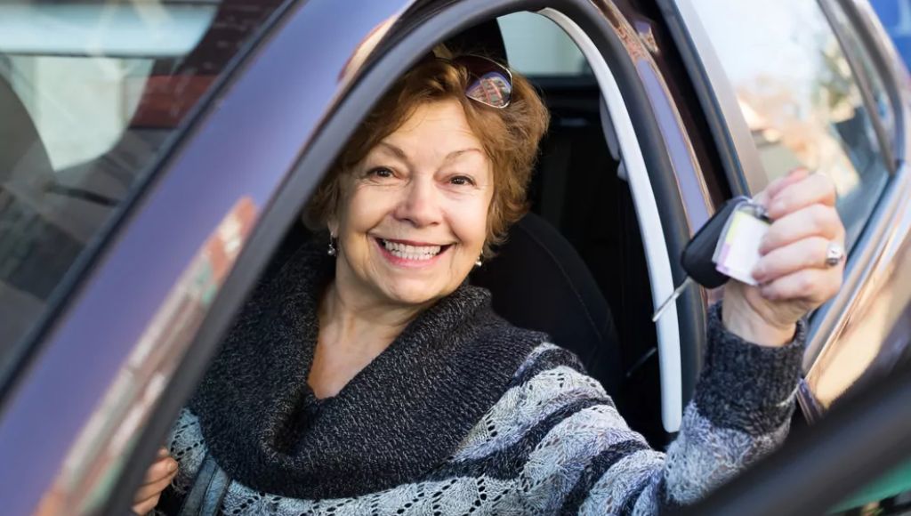 Idosa sorrindo para a foto dirigindo seu veículo, habilitada com a CNH para idosos.