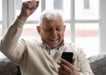 senhor sorridente comemorando com celular na mão