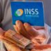 imagem com uma mão segurando o cartão do INSS e a outra as notas de 50 reais representando quanto tempo falta para me aposentar