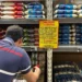 Homem olha gôndolas de arroz do supermercado, com uma placa de aviso.