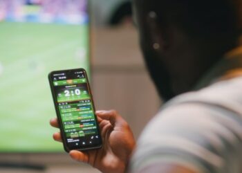 imagem com um homem vendo um jogo de futebol e usando o celular para fazer apostas no Brasil
