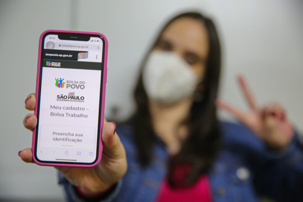 imagem com uma mulher com o celular na mão mostrando o aplicativo que faz o cadastro do Bolsa Trabalho.