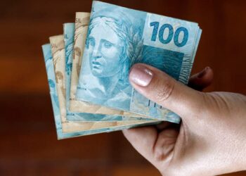 mão com dinheiro que cai com o pagamento do 13º salário do INSS
