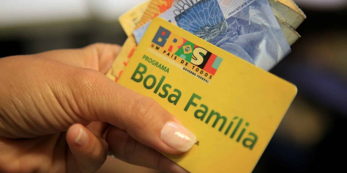 mão segurando o dinheiro e o cartão do Bolsa Família