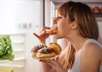 mulher na frente da geladeira comendo um doce