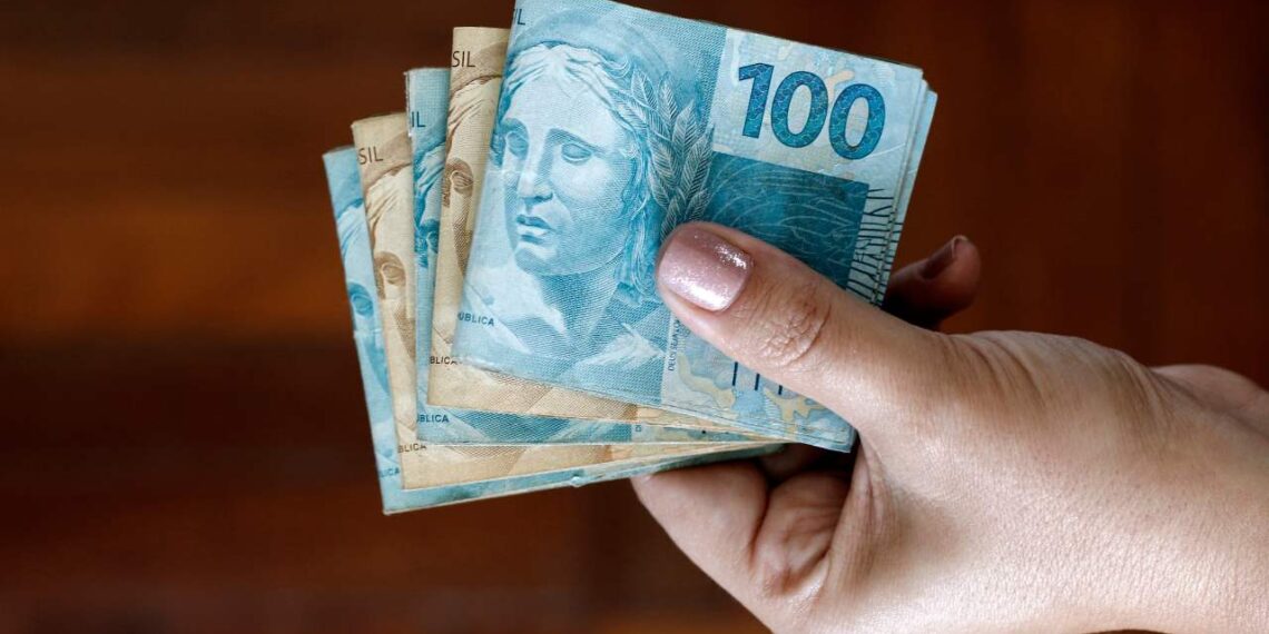 mãos segurando dinheiro que cai com o pagamento do 13º salário