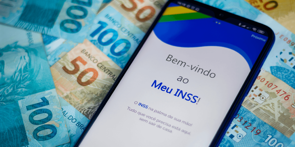 imagem mostra um celular com o aplicativo MEU INSS aberto com as boas vindas, e em baixo do celular algumas notas de dinheiro, notas de 100 e de 50 reais.