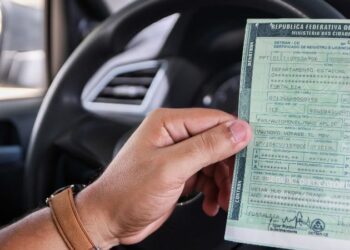 imagem de uma pessoa segurando o documento de IPVA dentro do carro